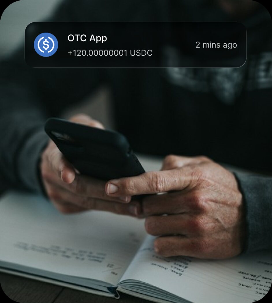 Hands holding a phone above a notebook, with an incoming USDC notification overlaid